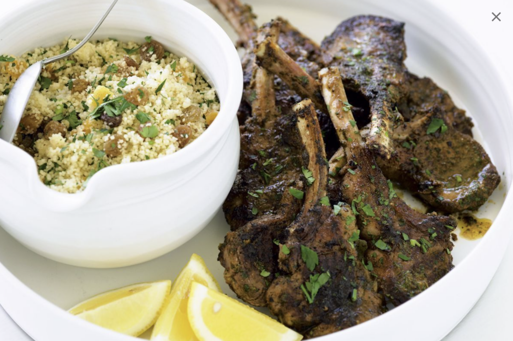 Moroccan braised lamb shank with couscous on a white plate with lemon garnishes